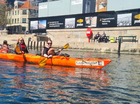 Kajakkers peddelen de kajaktocht Kopenhagen haven langs historische waterkantgebouwen