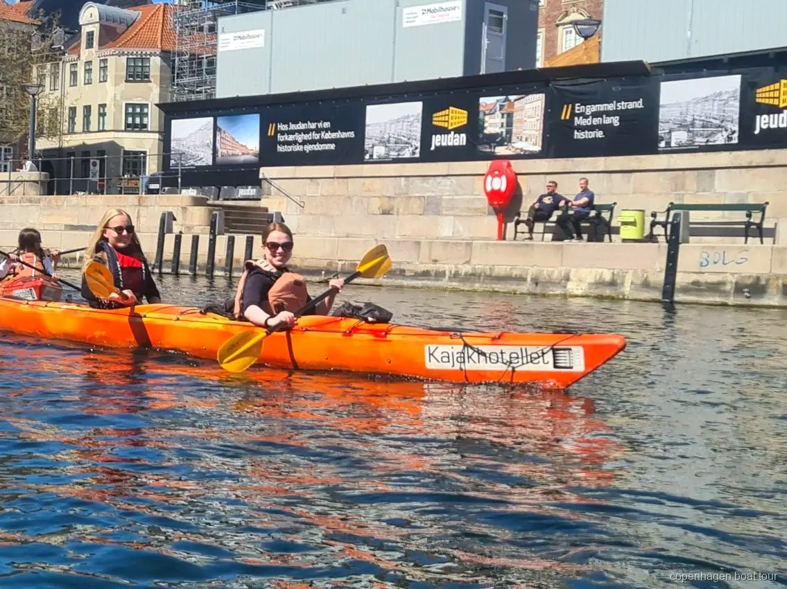 Kajakkers peddelen de kajaktocht Kopenhagen haven langs historische waterkantgebouwen